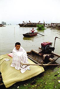 7月13日，淮河支流淝河大堤上，一村民裹着被单在船上过了一夜，家已经被洪水吞没